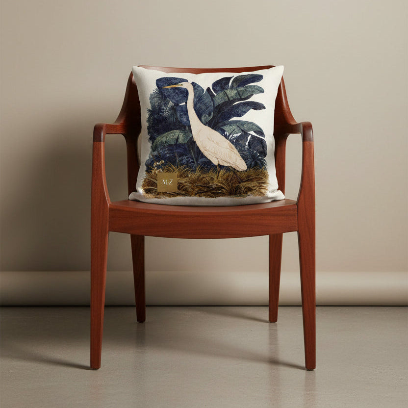 Photographie professionnelle extrêmement détaillée et de haute qualité d'un coussin mzelle design motif héron créole, disposé sur un fauteuil japonais moderne en bois de mahogany laqué, assise en bois, disposé contre un mur, dans un décor beige neutre.