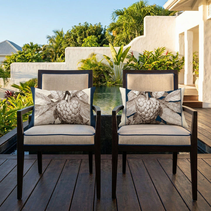Photo professionnelle de décoration d'intérieur, terrasse d'une villa créole baignée de soleil ,gros plan de face sur 2 chaises en wengé orné de chaque côté d'un coussin rectangle mzelle design motif pomme cannelle attier, en arrière plan placé devant une piscine sombre moderne à débordement, et jardin tropical.