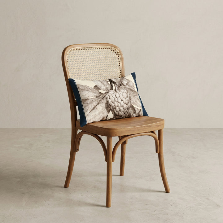 Photographie d'un grand coussin carré mzelle design motif fruit tropical attier, disposé sur un fauteuil de style créole, en bois précieux disposé sur un fond neutre, qualité studio photo. 
