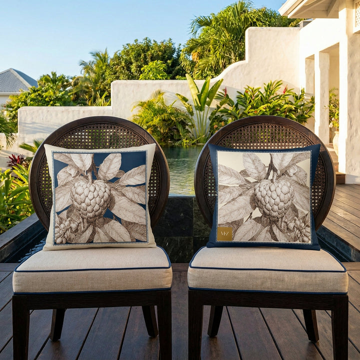 Photo professionnelle de décoration d'intérieur, terrasse d'une villa créole baignée de soleil ,gros plan de face sur 2 chaises en wengé orné de chaque côté d'un large coussin mzelle design motif pomme cannelle attier, en arrière plan placé devant une piscine sombre moderne à débordement, et jardin tropical.