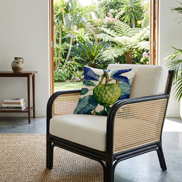 Photographie professionnelle d'aménagement intérieur, mettant en scène un superbe fauteuil de style contemporain en rotin teinté foncé, orné d'un grand coussin carré mzelle design motif fruit tropical,  l'assise et le dossier sont en tissu texturé lin beige, avec cannage écru sur les côtés, exposé dans un lodge tropical lumineux, vue jardin.