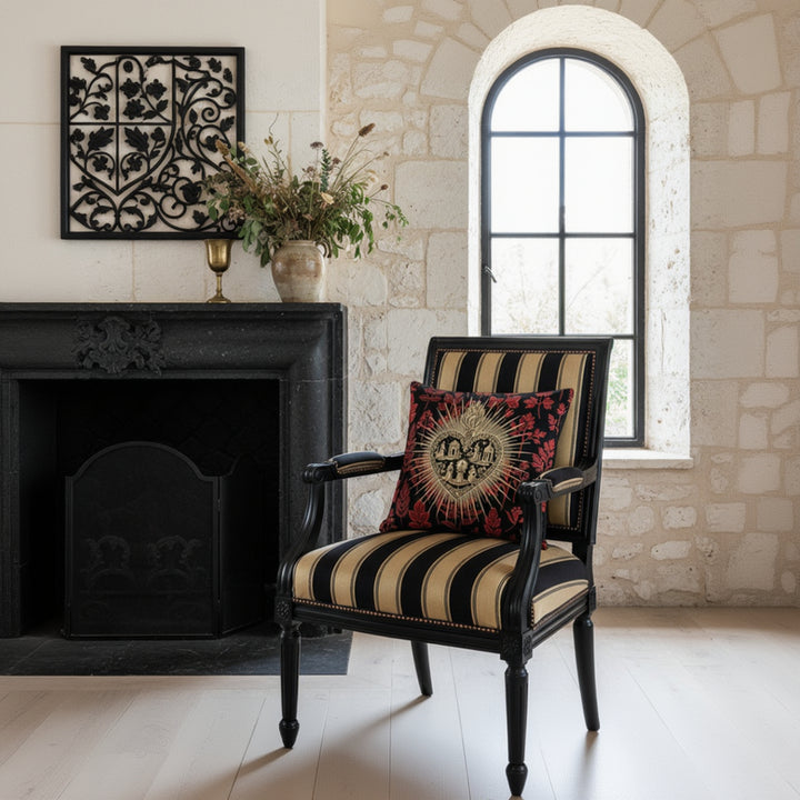 Photographie professionnelle de décoration d'intérieur, villa française inspirée de l'esthétique Castlecore avec une chaise Empire aux assises à rayures noir et dorées et rivets cuivrés, ornée d'un large coussin carré. 