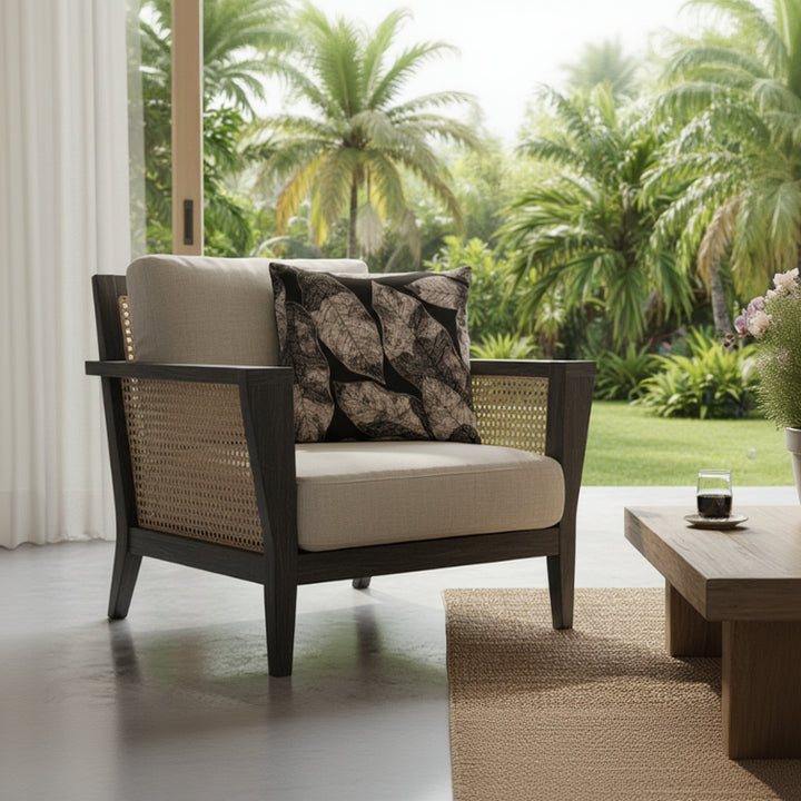 Photographie professionnelle d'aménagement intérieur, mettant en scène un superbe fauteuil de style contemporain en rotin teinté foncé, orné d'un grand coussin carré mzelle design motif tropical,  exposé dans un lodge tropical lumineux, vue jardin.