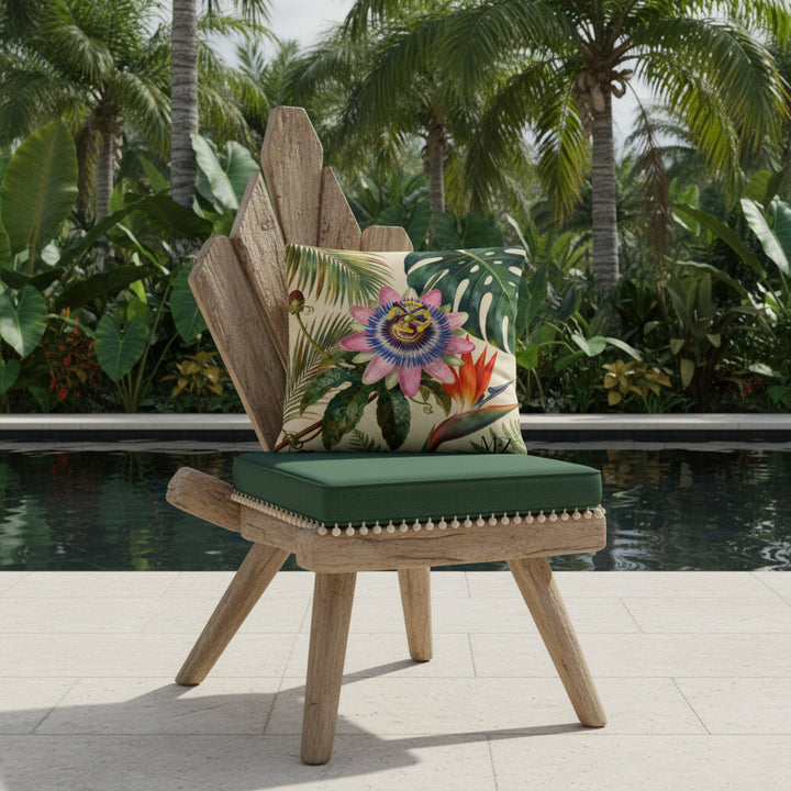 Photographie professionnelle vue d'un grand coussin carré motif fleur de passiflore, disposé sur une chaise au design original et contemporain en bois flotté, sans accoudoirs, dossier en bois triangulaire, assise vert foncé finitions petits pompons écrus, placé devant une piscine sombre moderne à débordement et plantes exotiques. 