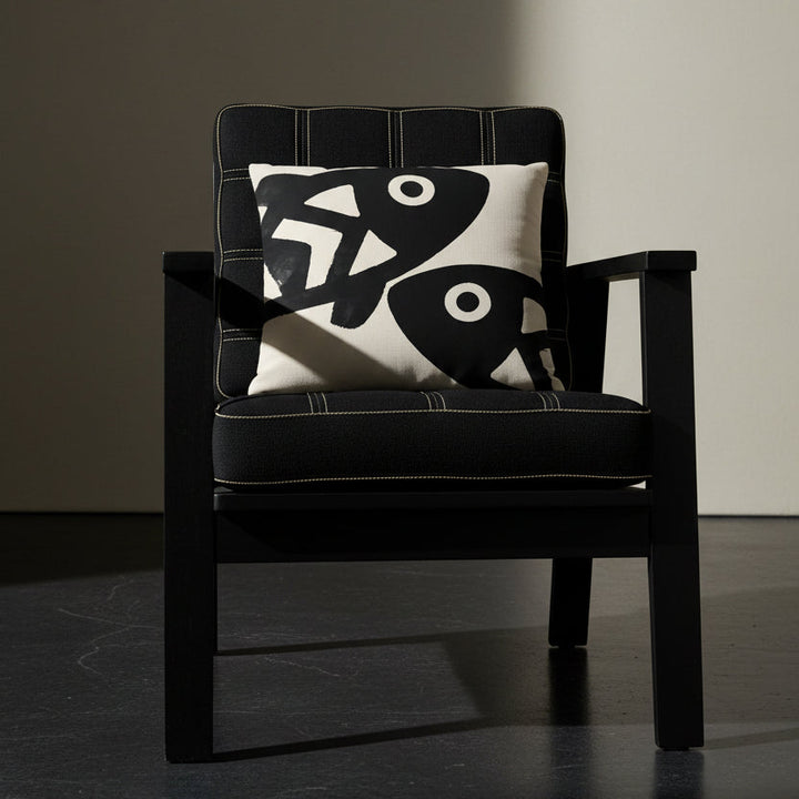 Photographie professionnelle qualité studio, d'un coussin carré mzelle dsign motifs poissons disposé sur une chaise japonaise sans accoudoirs, dossier en tissu noir surpiqué de fil écru, structure épaisse, disposé dans décor écru neutre, sol en béton ciré noir.