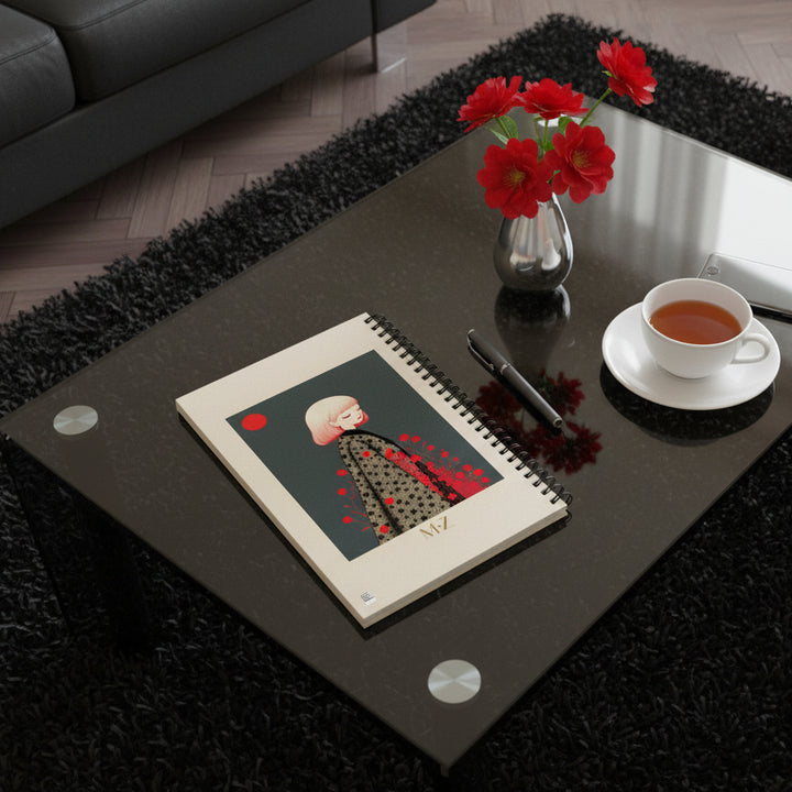 photo de décoration vue en plongée, salon cosy, le Carnet posé sur une table basse en plexiglass fumée, à côté d'une tasse de thé, un stylo, un smartphone et des fleurs rouges dans un petit vase argenté.